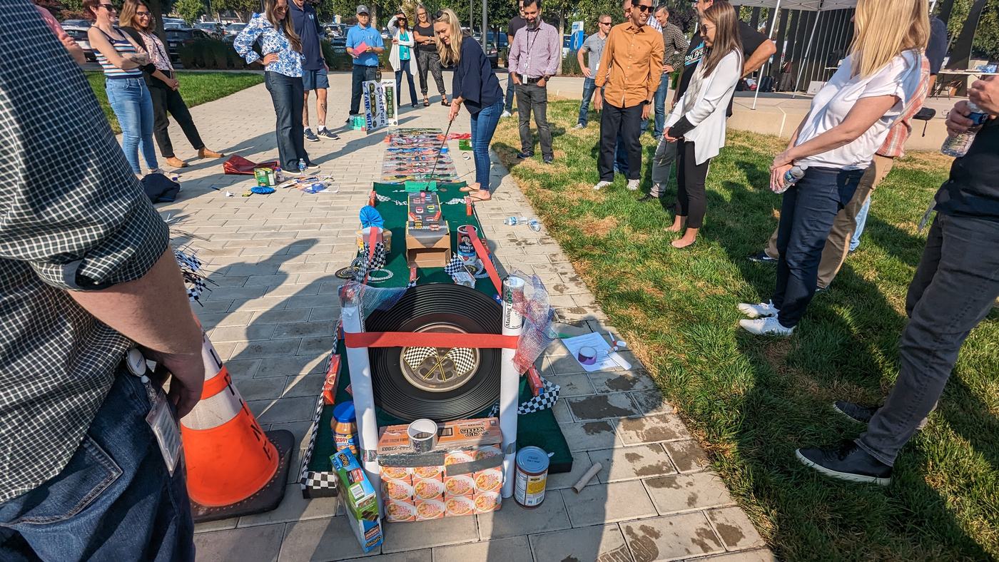 A team watches a putt through a long food-can obstacle course